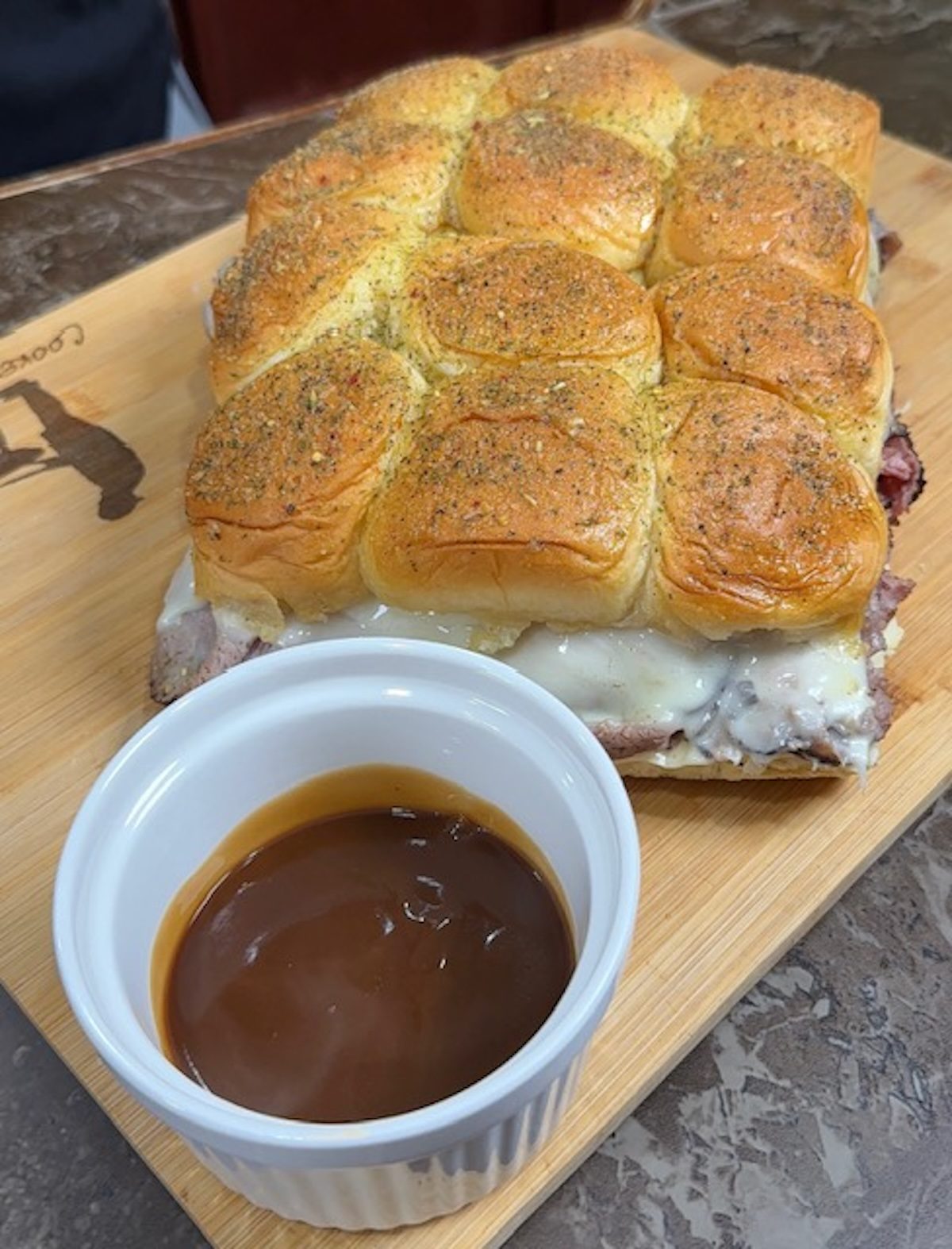 Beef and gravy sliders on a cutting board with a white ramekin of gravy in front.