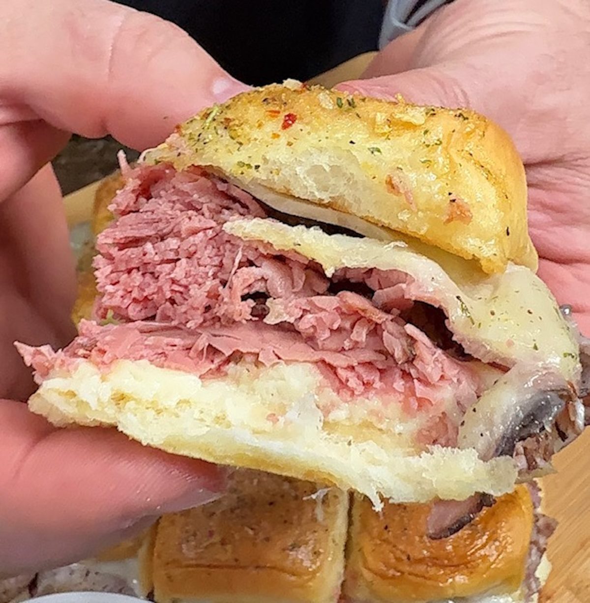 Two hands are lifting up a roast beef and cheese slider.