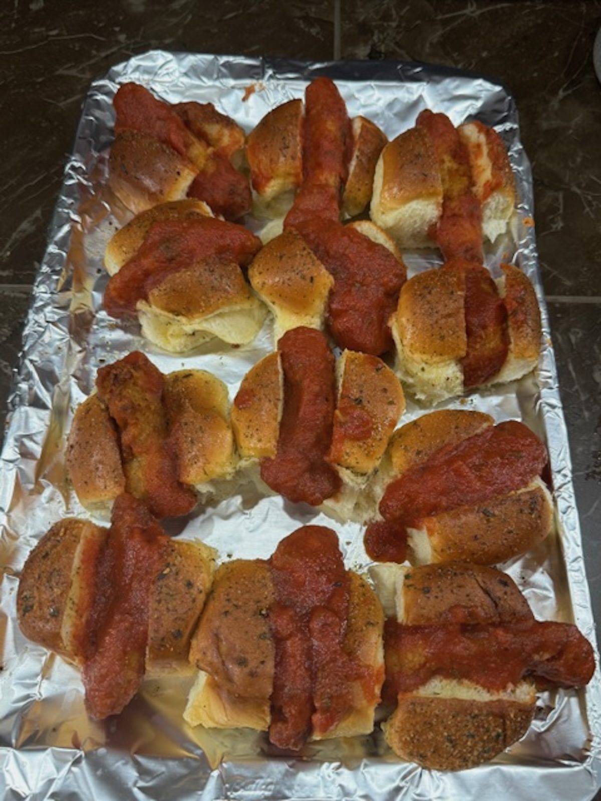 Chicken fingers are dipped in marinara sauce and placed in between slider buns on a foil-lined baking sheet.