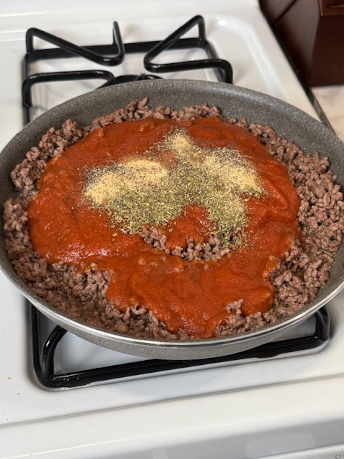 Red sauce and spices are added to ground beef in a skillet.