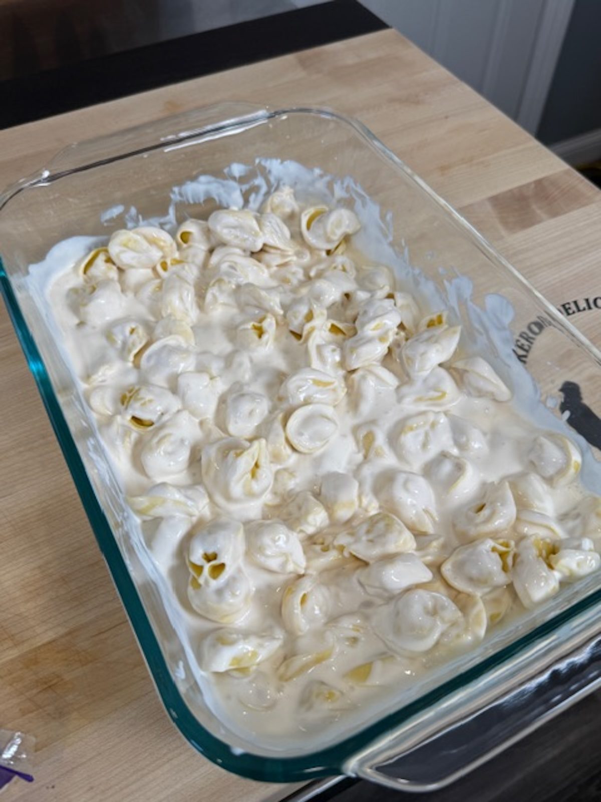 Tortellini is added to the Alfredo sauce in the casserole dish.