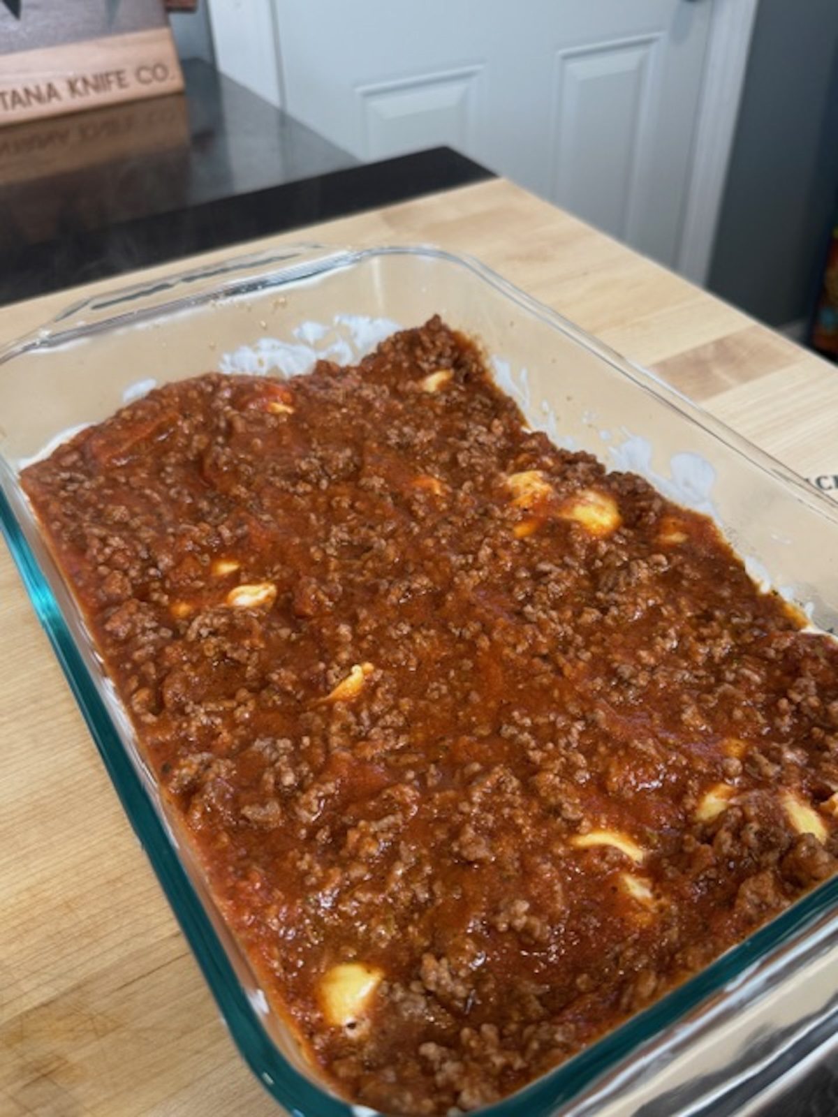 Meat sauce is added on top of the tortellini in the glass casserole dish.