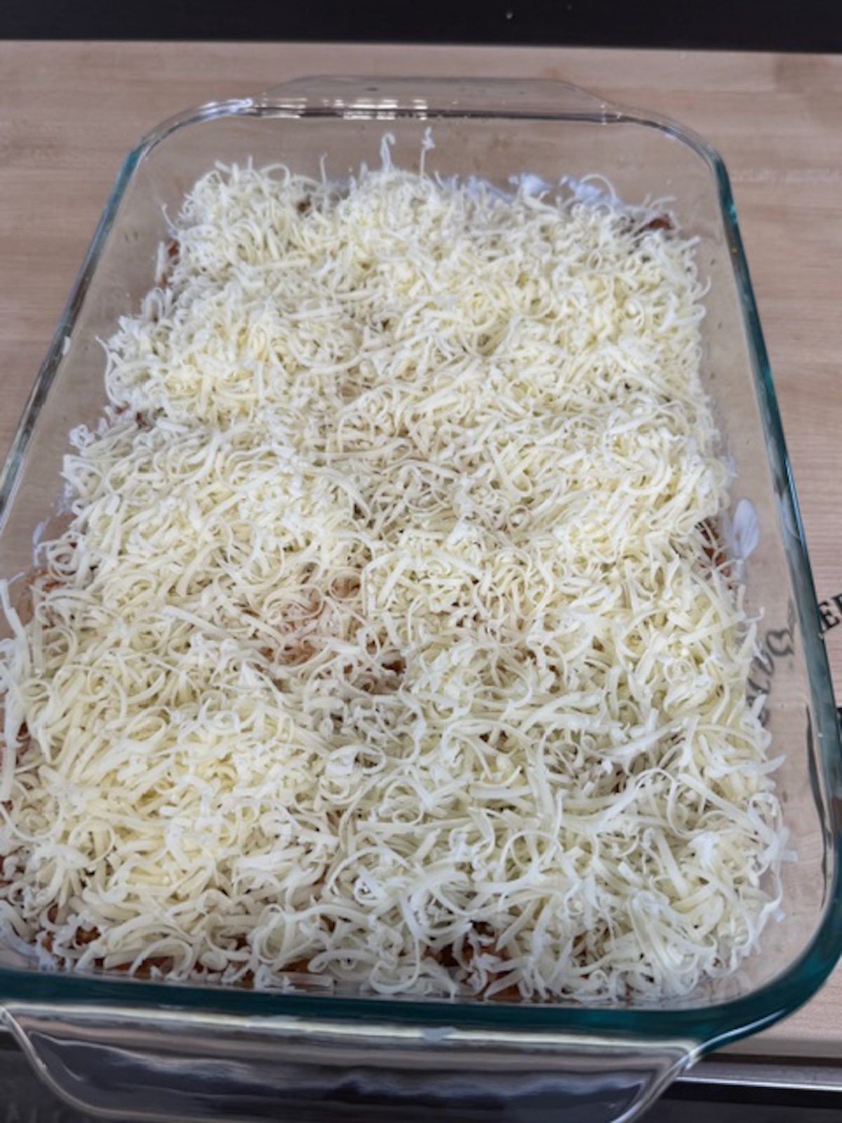 Shredded mozzarella is added on top of the million dollar tortellini bake in the glass casserole dish.