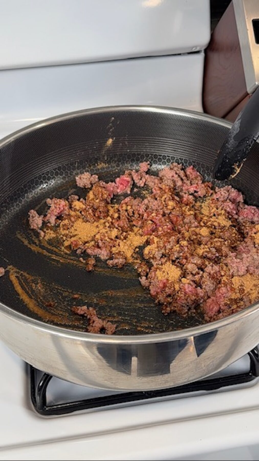 A skillet with ground beef and taco spices browning on the stove.
