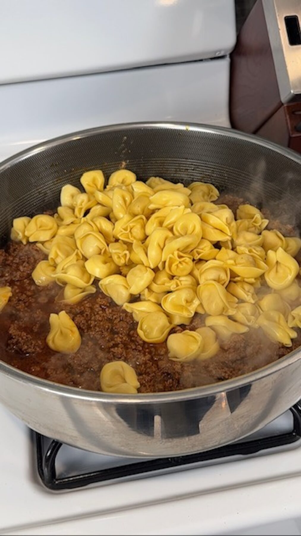 Tortellini added to the ground taco meat in a skillet on the stove.