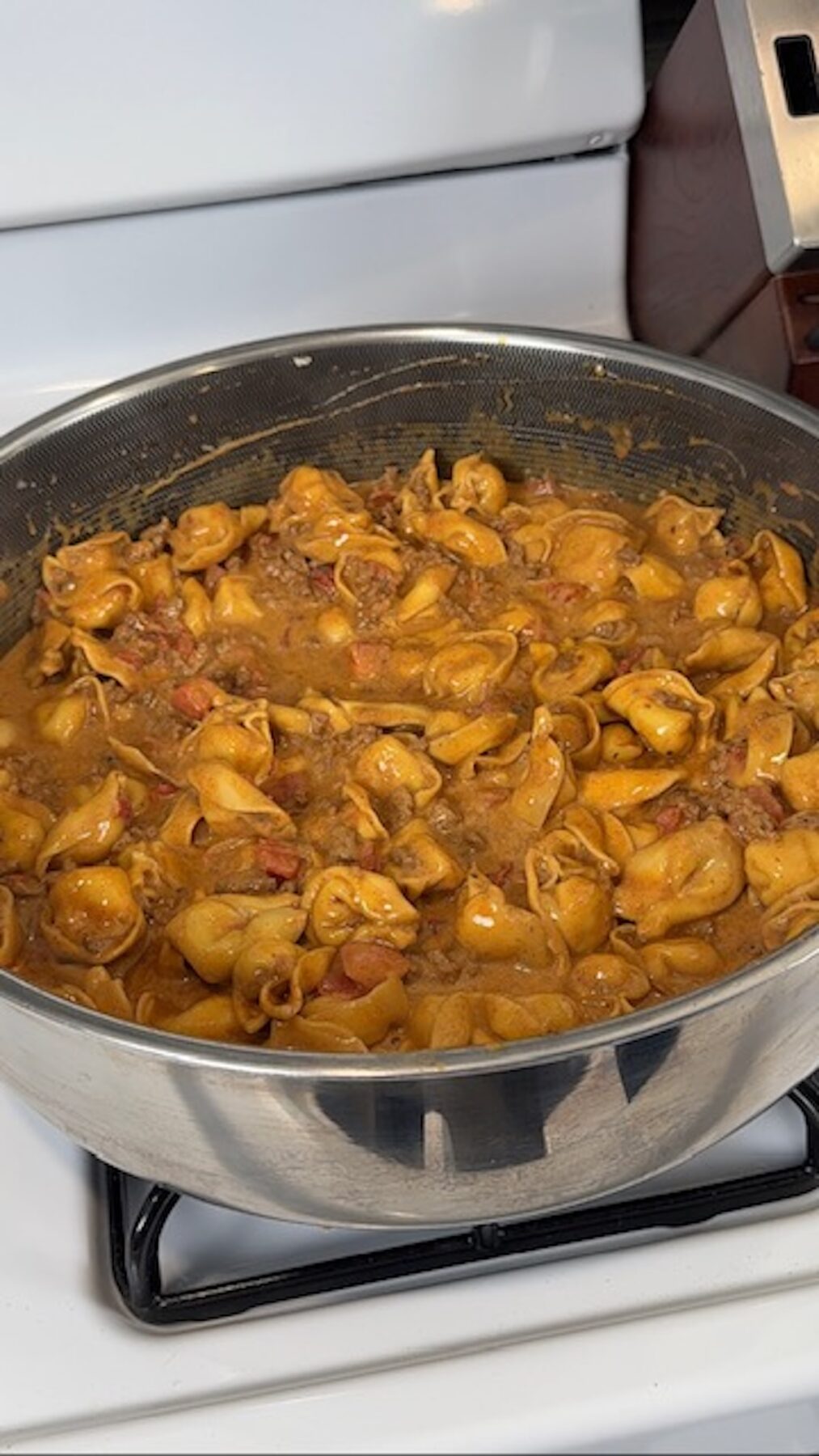 Taco tortellini with sour cream and queso added to the sauce in a skillet on the stove.