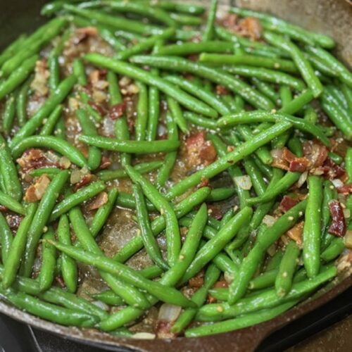 Green beans are added to the skillet with bacon and onions.