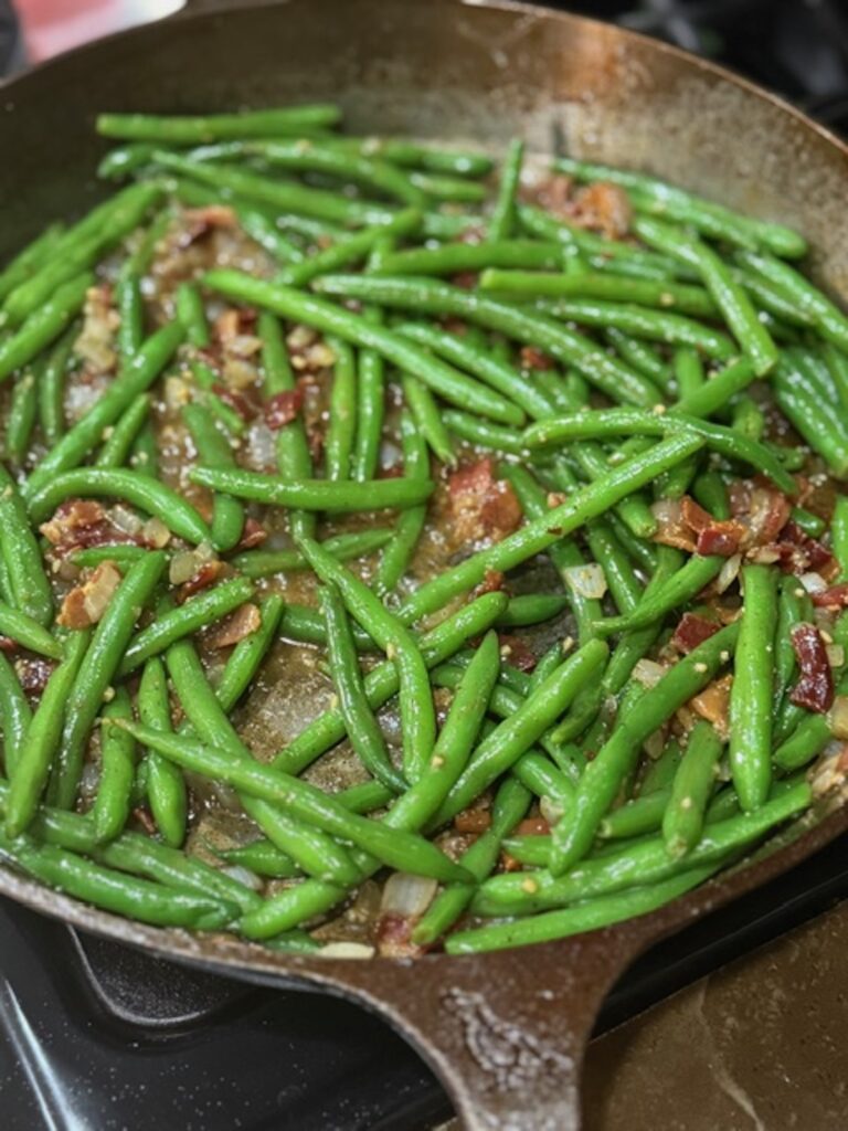 Green beans are added to the skillet with bacon and onions.