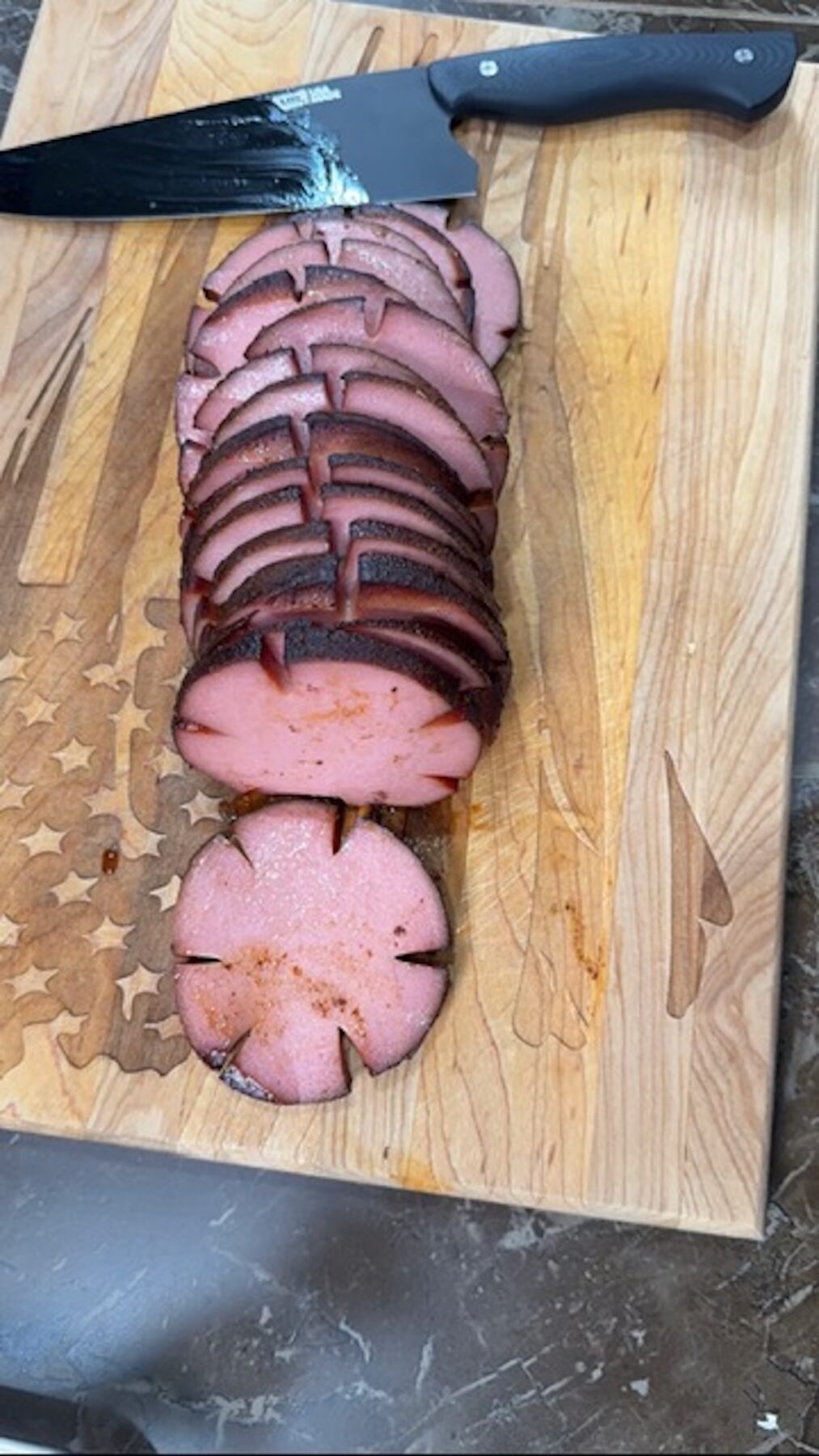 Bologna is thinly sliced on a cutting board with a knife.
