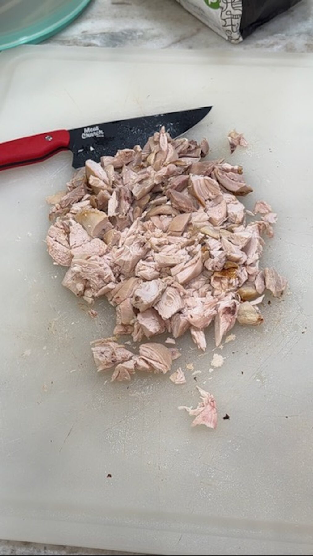 Chopped chicken on a cutting board with a knife.