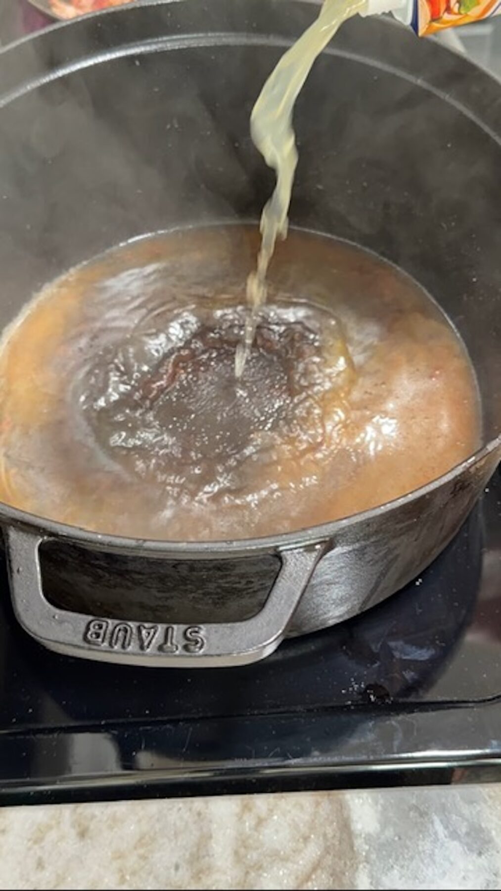 A dutch oven with broth being poured in.