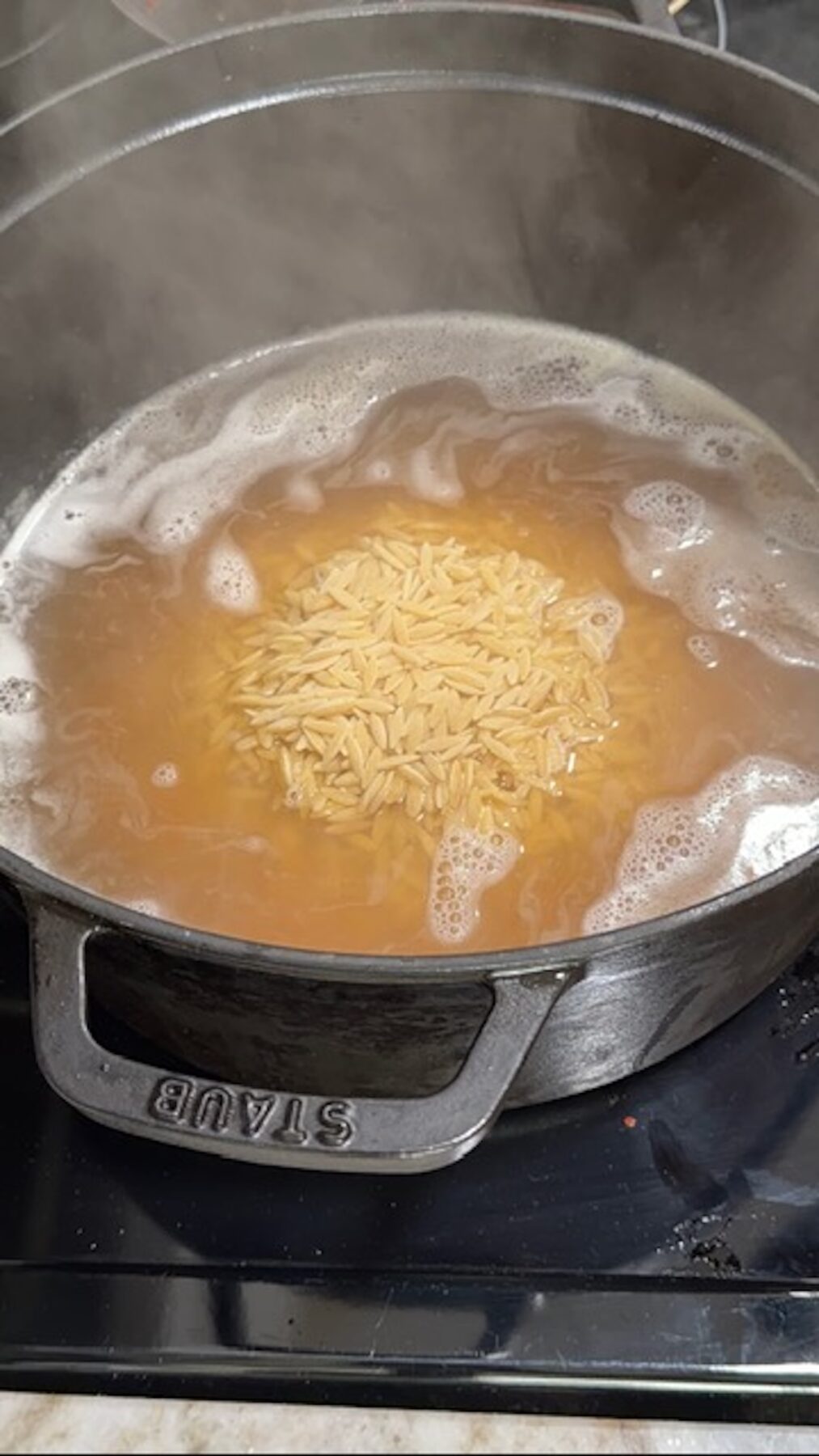 Orzo cooking in chicken broth in Dutch oven.