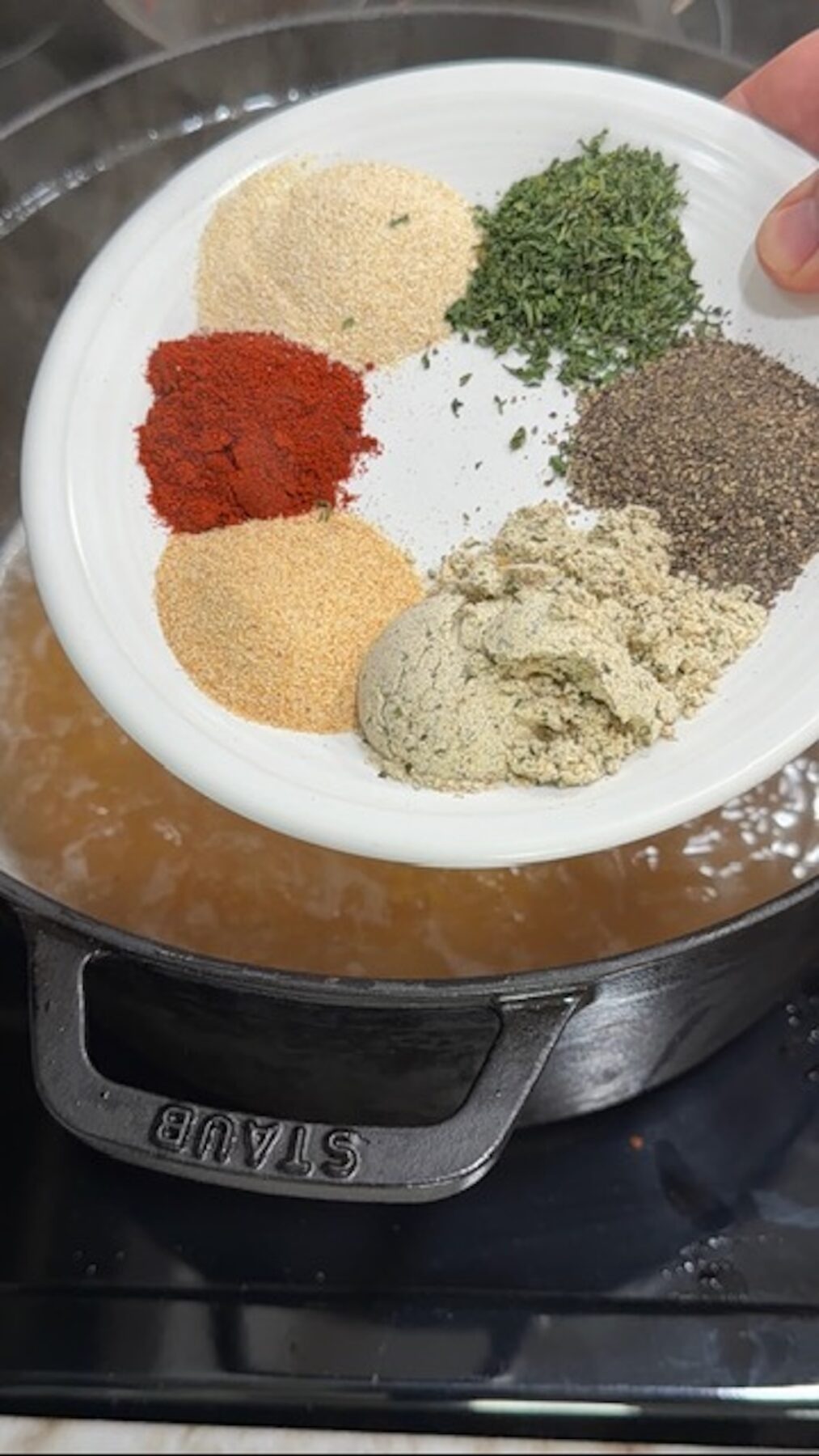 A white plate of dried spices over a dutch oven with chicken broth.