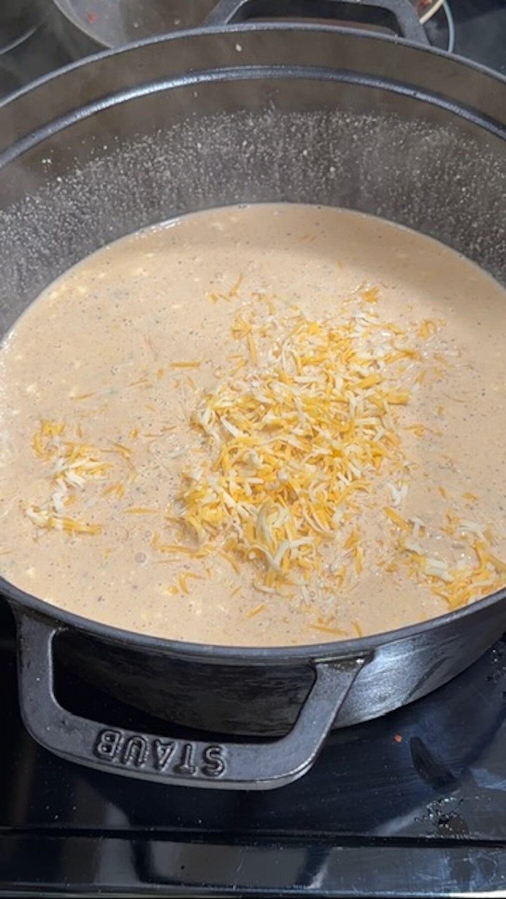 A dutch oven with crack chicken soup and shredded cheese blend on top.