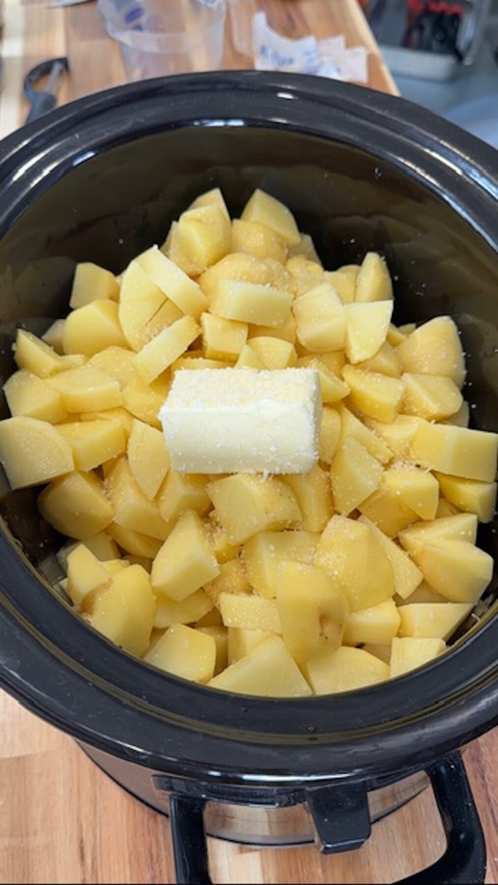A slow cooker with cubed potatoes and part of a stick of butter.