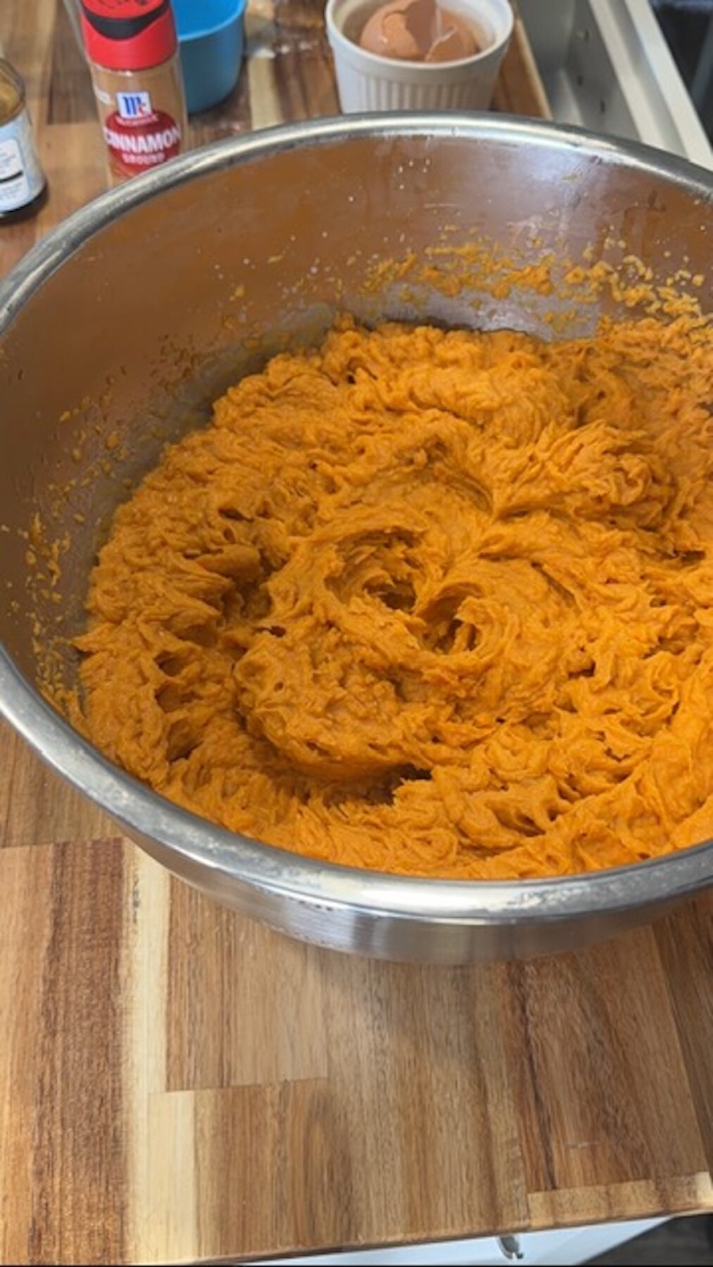 Mixed sweet potato casserole filling in a metal bowl on a wooden cutting board.