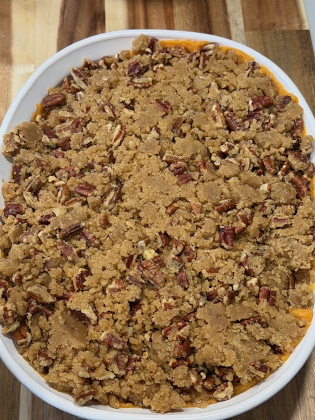 Sweet potato casserole with pecan topping in a white baking dish on a wooden cutting board.