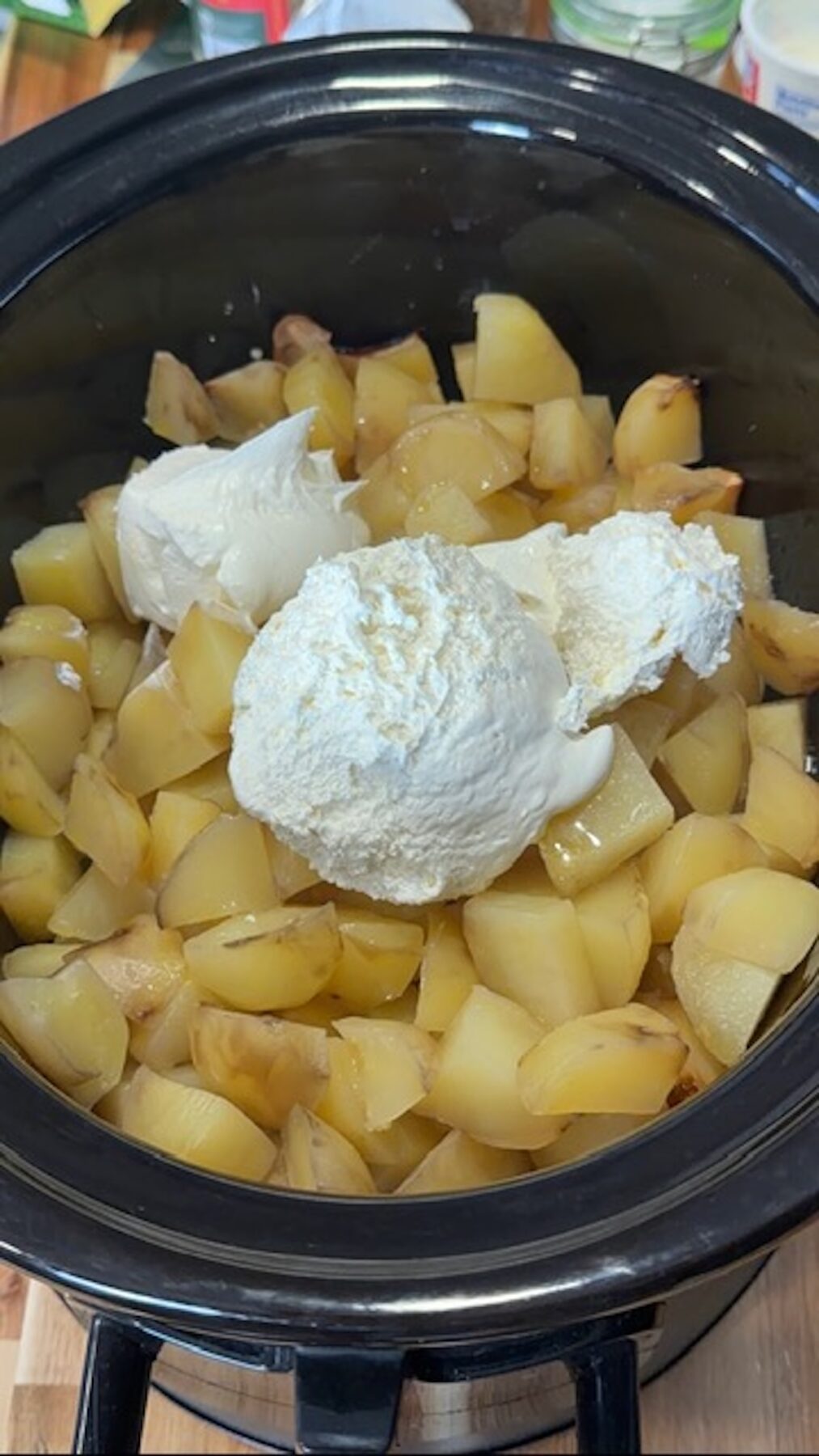 A slow cooker with boiled cubed potatoes, sour cream, and whipped cream cheese.