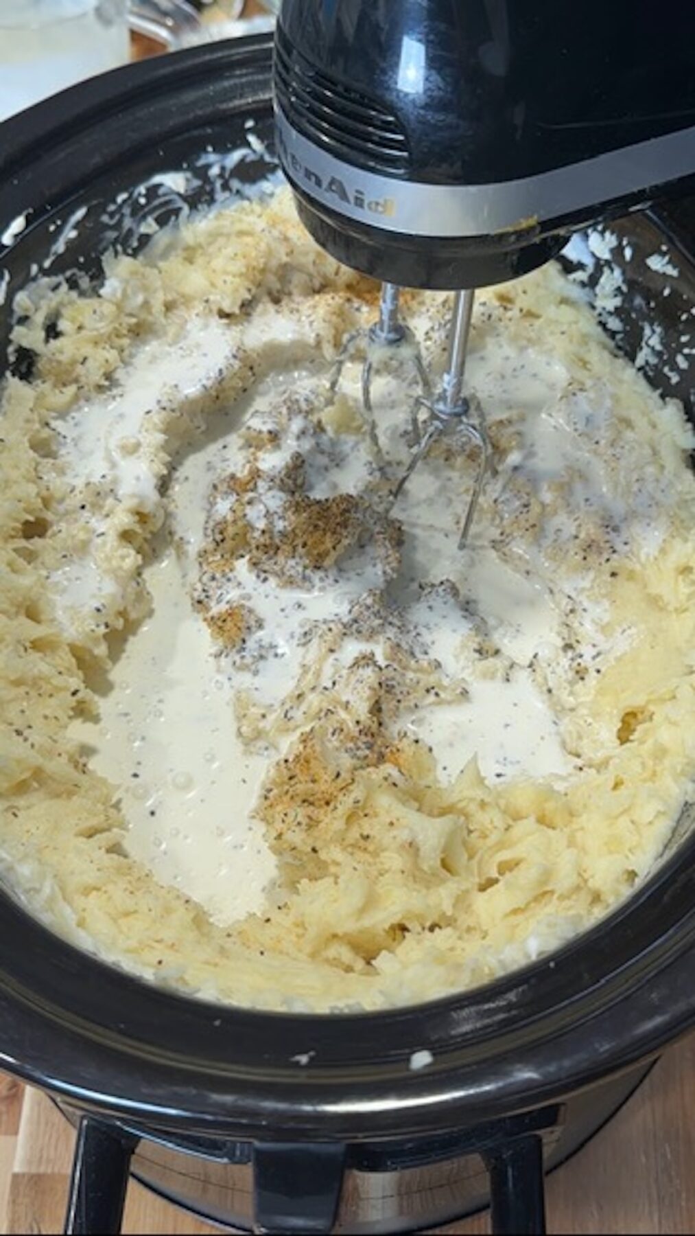 A hand mixer is mixing the slow cooker mashed potatoes.