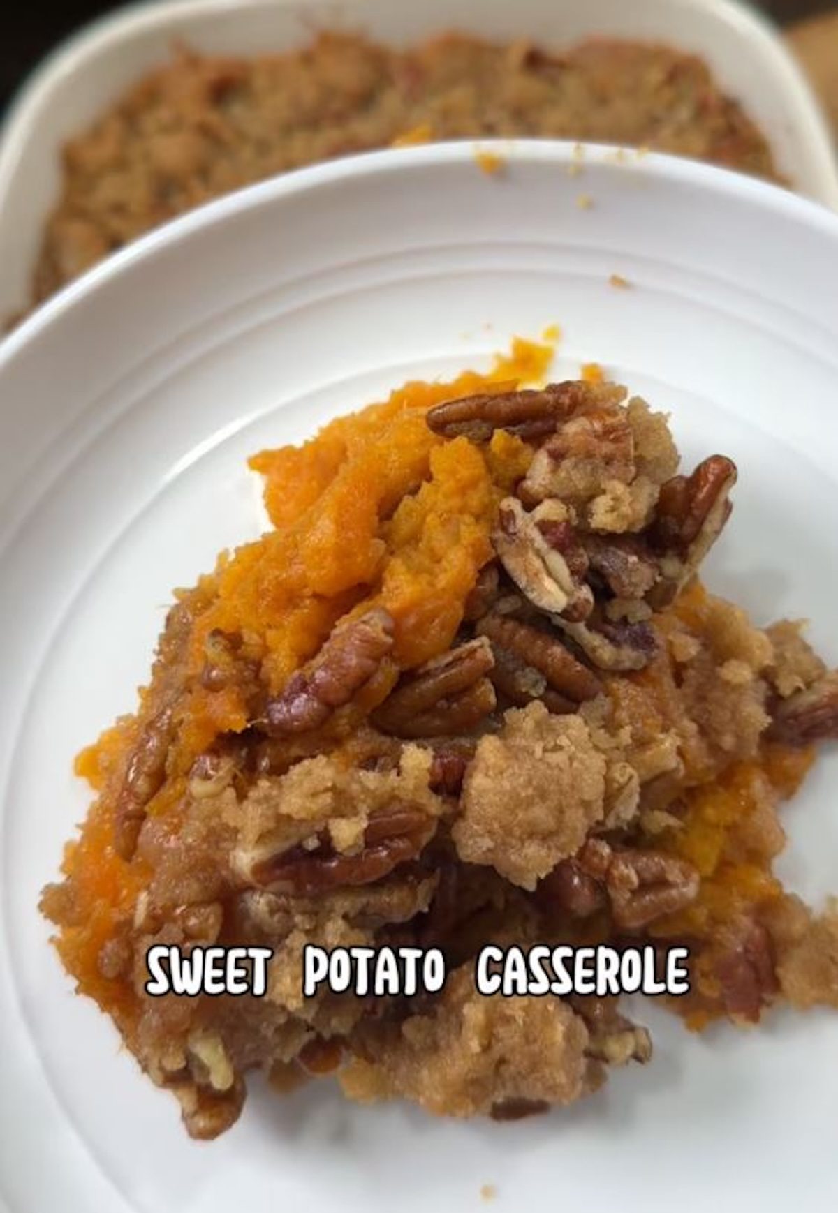 A serving of sweet potato casserole with pecan topping on a white plate.