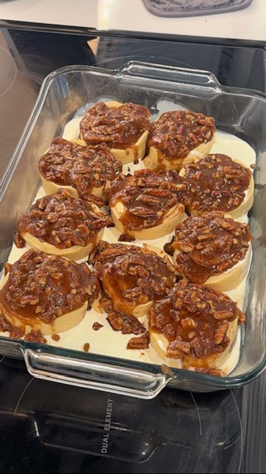 Cinnamon rolls in a glass baking dish covered with cream, caramel, and pecans before baking.