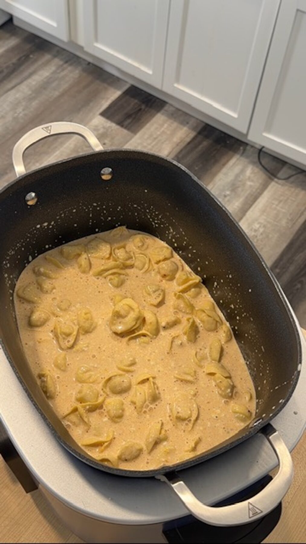 Slow cooker tortellini and cheese in the black crockpot bowl.