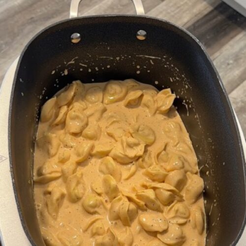 Slow cooker tortellini and cheese in a black crockpot bowl.
