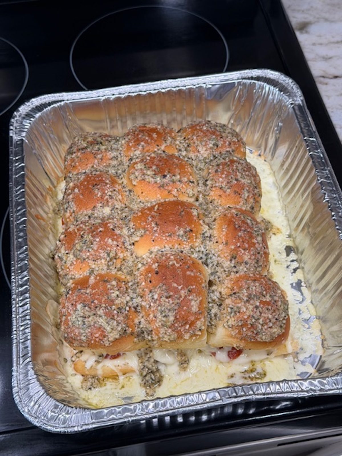 Baked pepperoni pizza sliders in a foil tray.