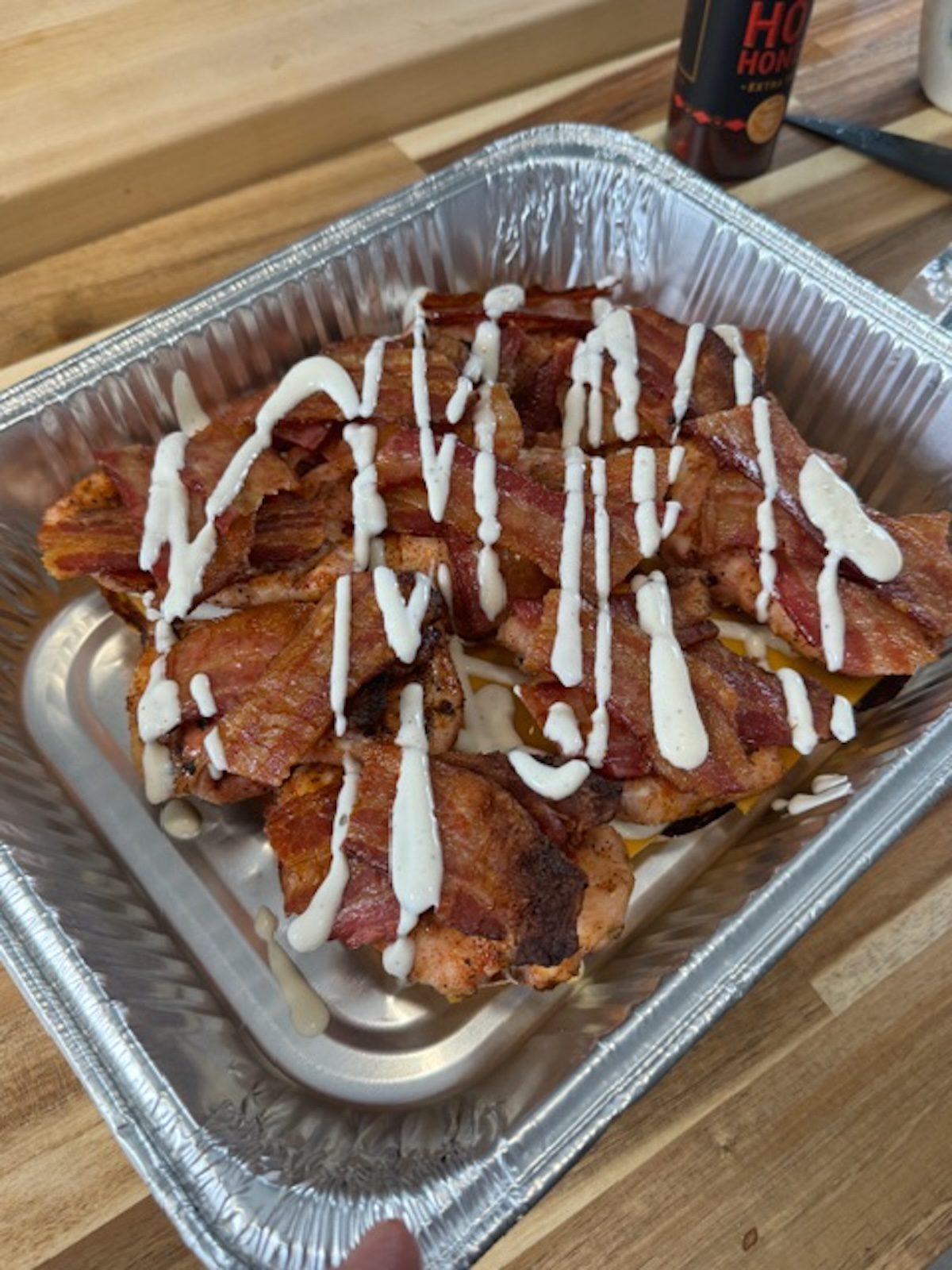 A silver pan with grilled chicken and ranch drizzled over the top.