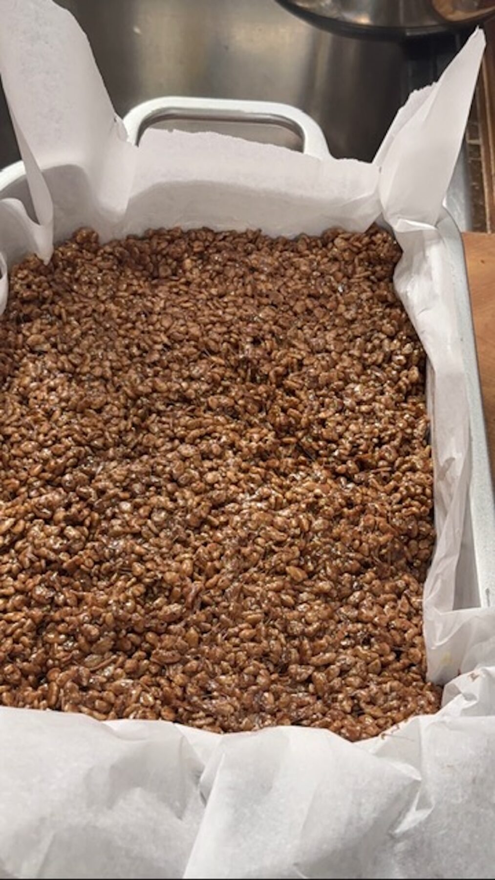 A baking dish with chocolate rice krispie treats pressed in to cool with parchment paper.