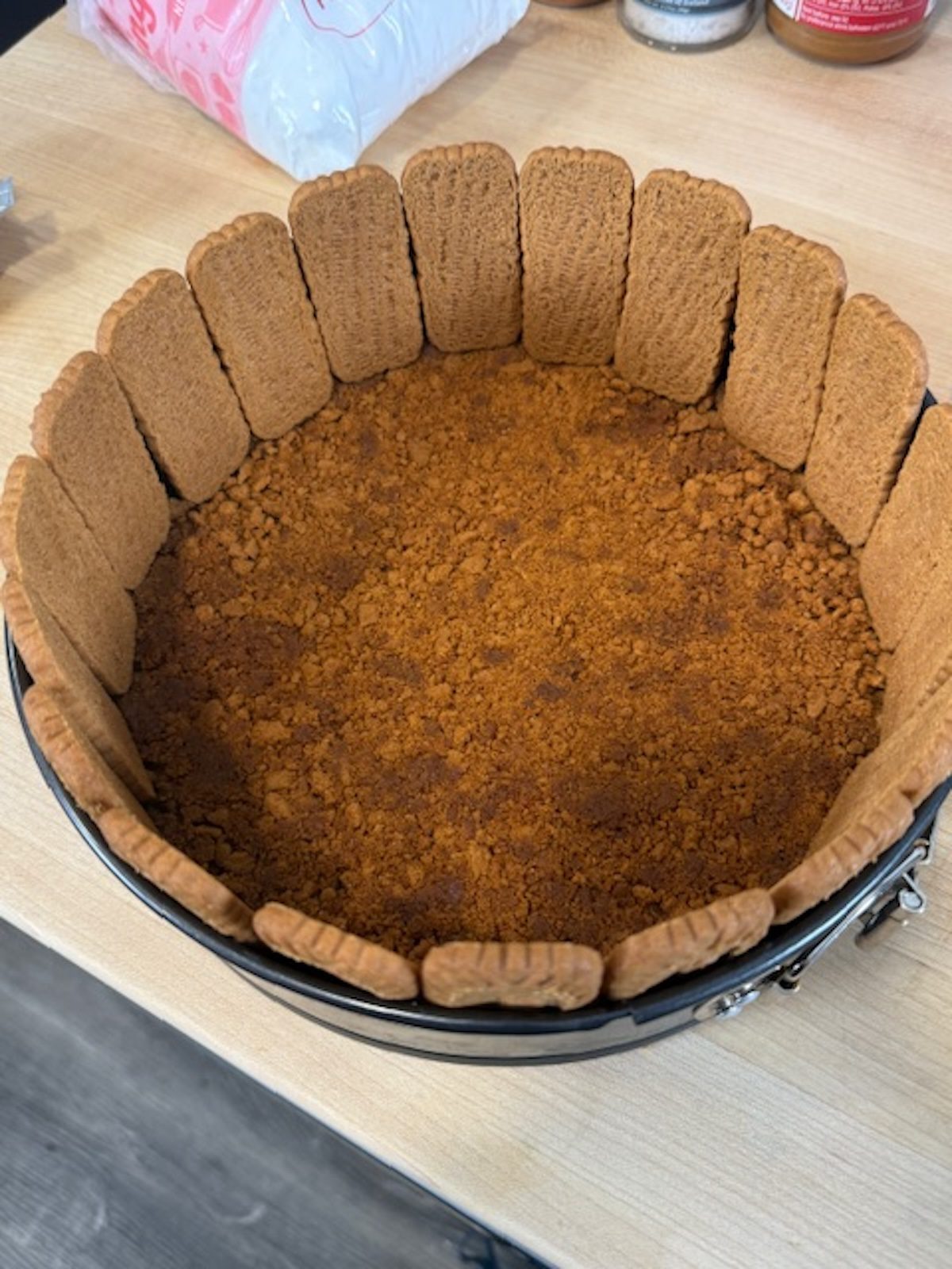 A cake pan lined with Biscoff cookies with cookie crumb crust in the bottom.