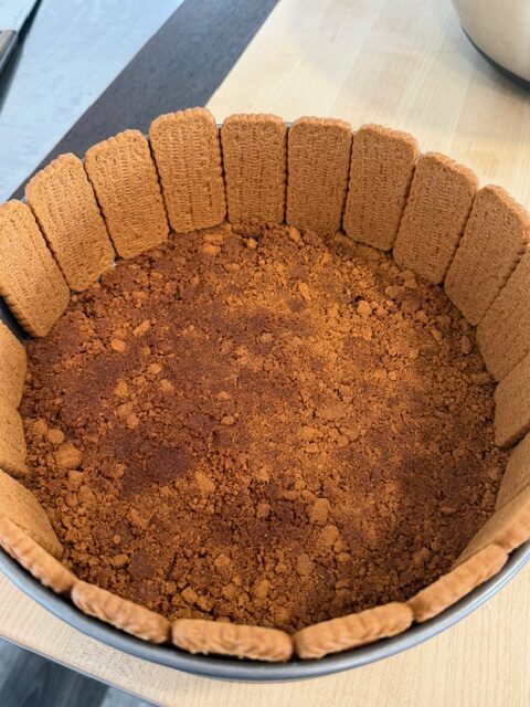 Biscoff cookies lined around the rim of a cake pan with crushed cookies in the bottom.