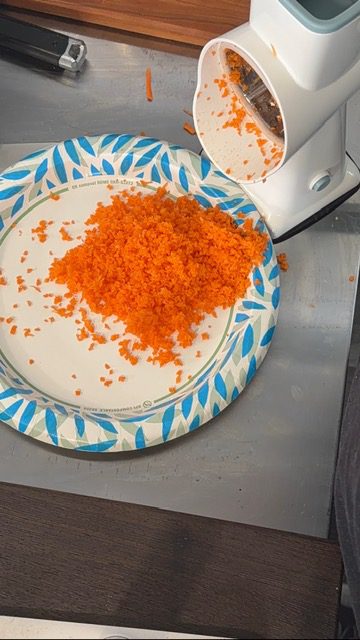 Grated carrots on a paper plate coming out of a grater.