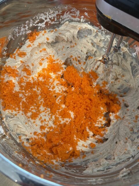 A hand mixer whipping grated carrots into carrot cake cheesecake.