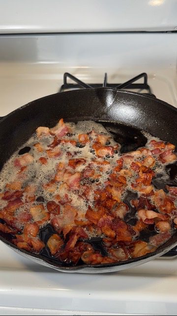 Bacon cooking in a cast iron skillet on the stovetop.
