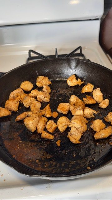 Chicken cooking in the bacon fat in a cast iron pan on the stovetop.