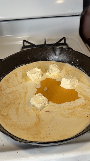 A cast iron pan with heavy cream and butter for crack chicken pasta.