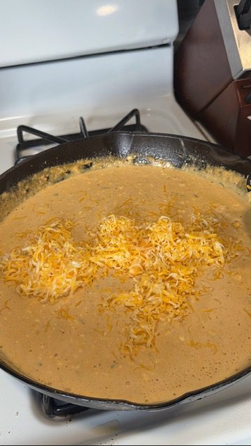 Cheese added to crack chicken pasta sauce in a cast iron skillet on the stovetop.