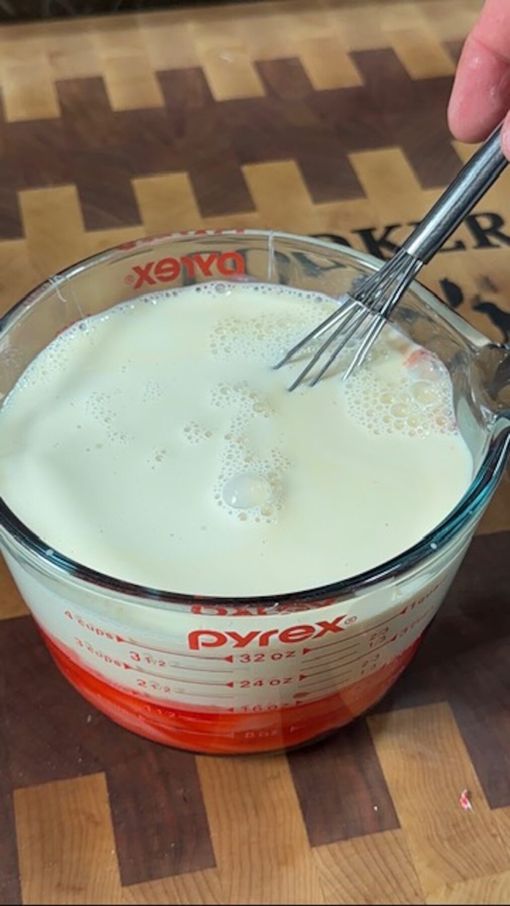 A hand whisking jello and milk in a glass measuring cup.