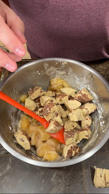 A metal bowl with cubed biscuit pieces and apple pie filling. A red spatula is resting on the side of the bowl.