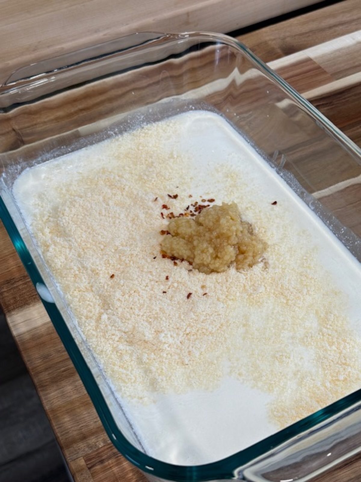 A glass baking dish with cream, garlic, and spices.