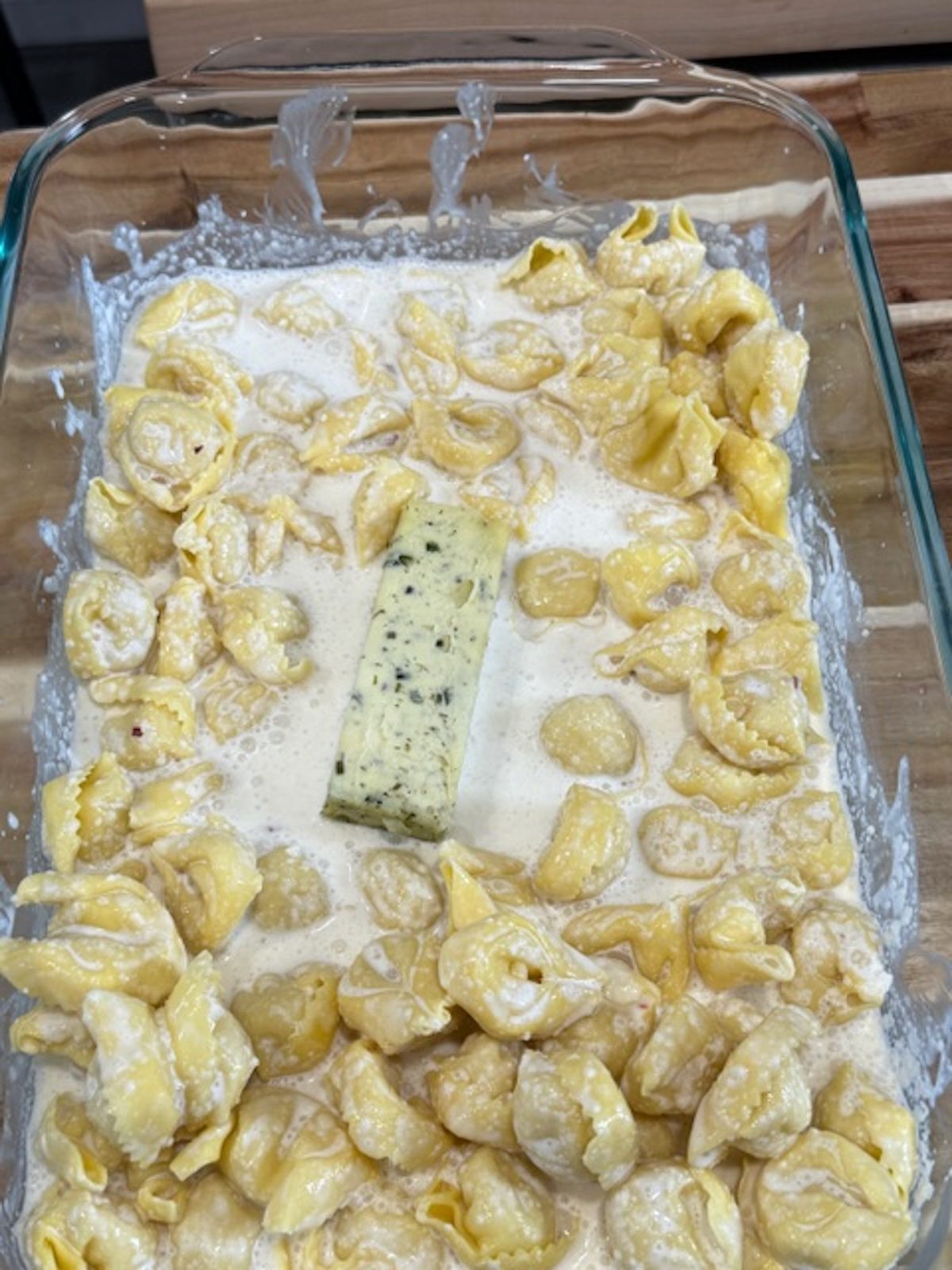A glass baking dish with cream, tortellini, and herb butter.