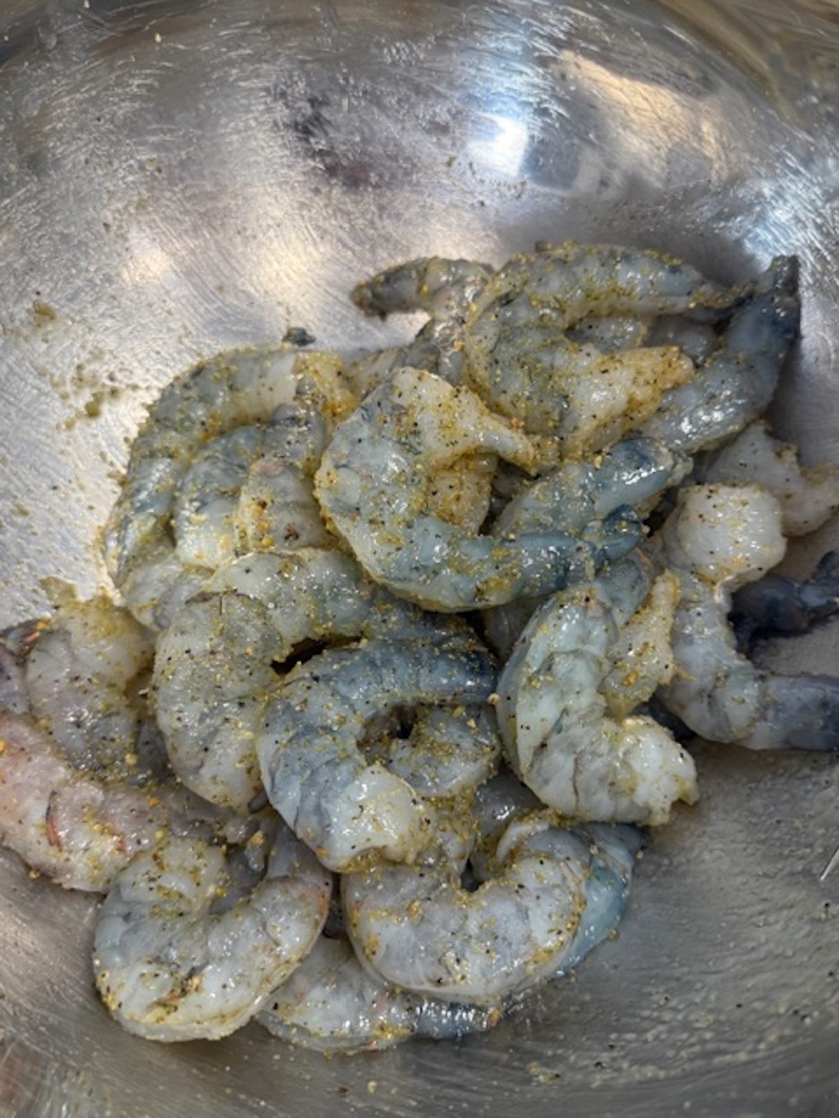 A metal bowl with shrimp tossed in spices.