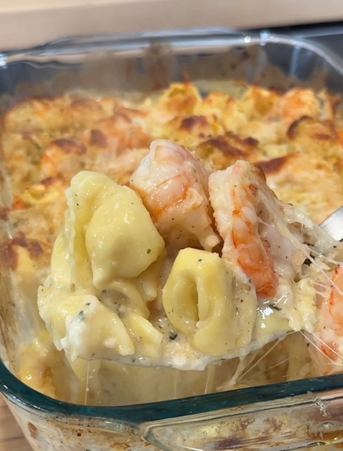 A spoon scooping out baked shrimp and tortellini.