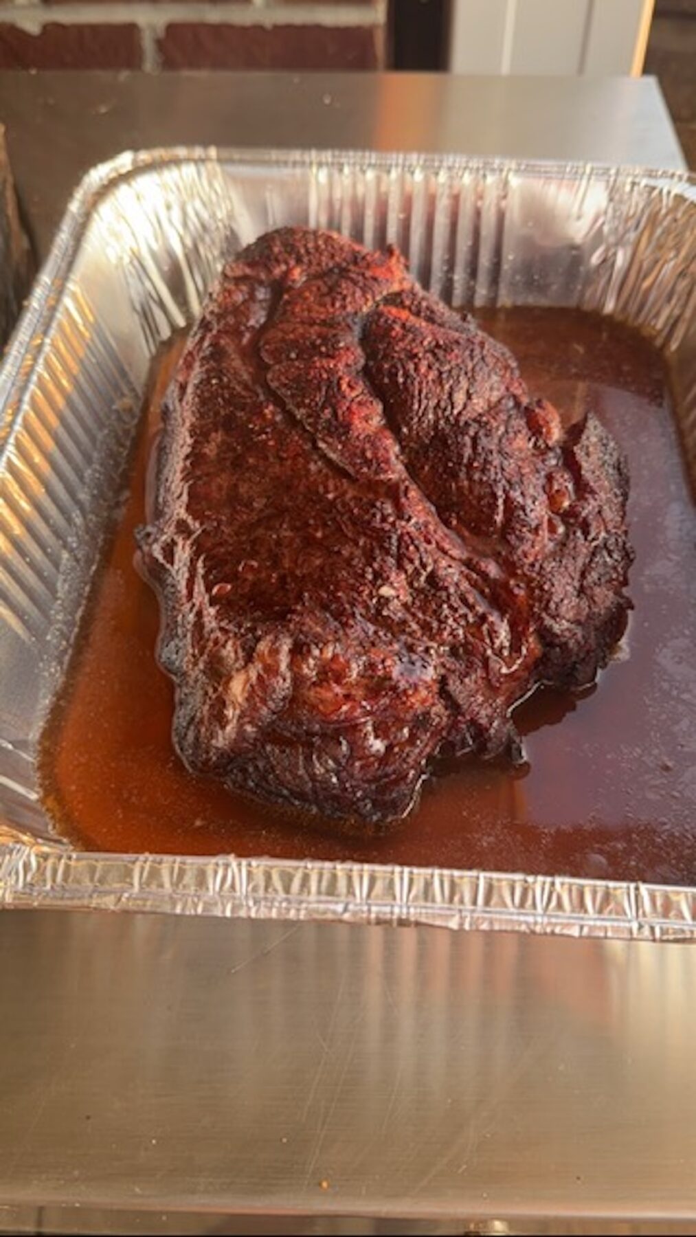 cooked and smoked bbq pulled beef unshredded sitting in aluminum pan in juices and liquid