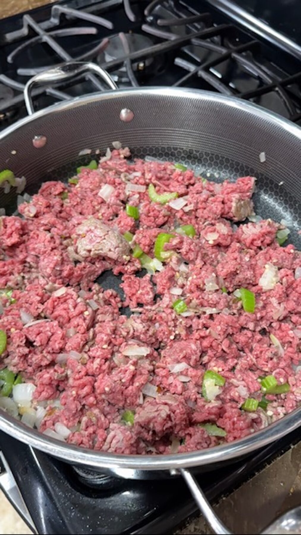 Ground beef, onions, and celery cooking in a pan.