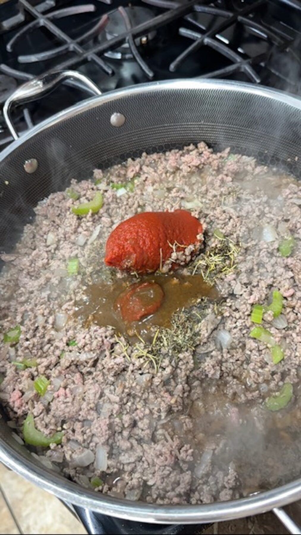 Beef, tomato paste, celery, onion, and spices cooking in a skillet.