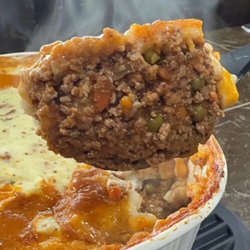 A big spoonful of cottage pie with the baking dish in the background.