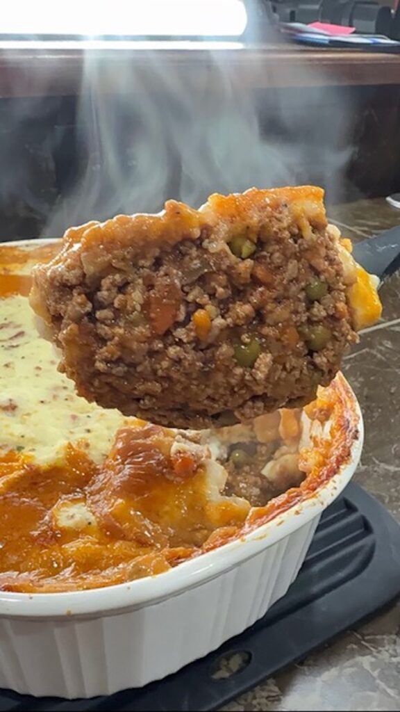 A big spoonful of cottage pie with the baking dish in the background.