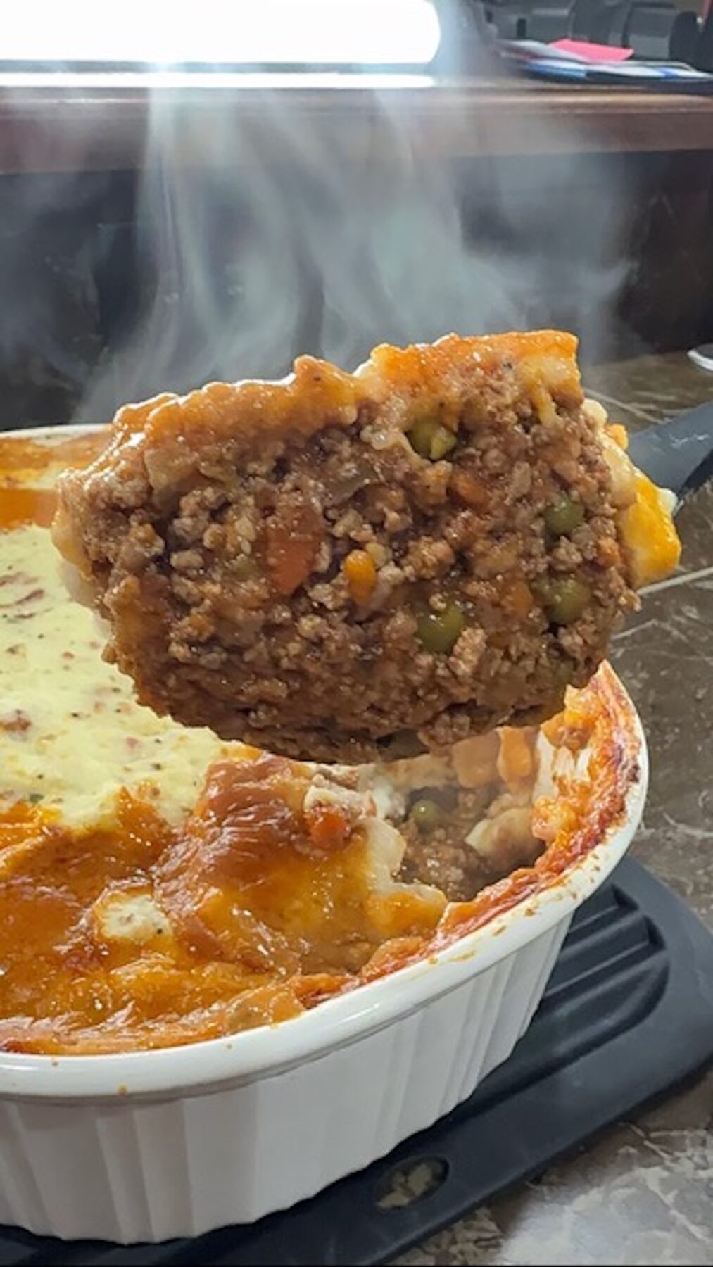 A big spoonful of cottage pie with the baking dish in the background.